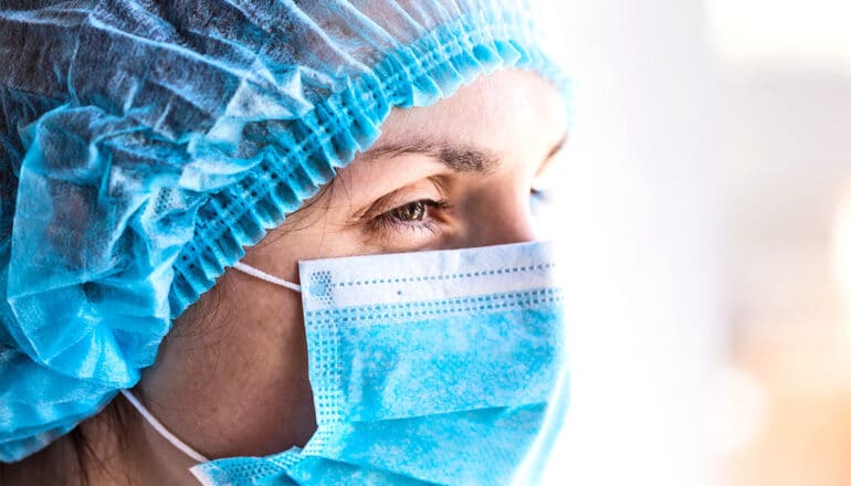 A doctor wears a hair net and face mask.