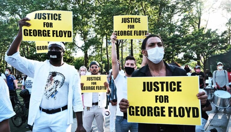 Protestors hold signs that read "Justice for George Floyd" while gathered at a park.