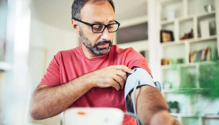 A man checks his blood pressure at home with a cuff device.