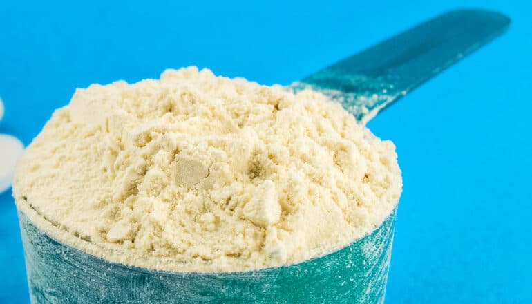 A measuring cup of supplement powder against a white background.