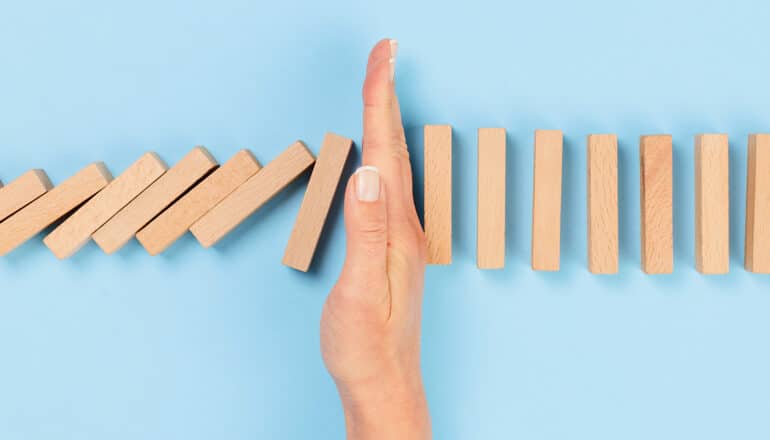 A woman puts her hand in between a row of fallen dominoes and a row yet to fall.