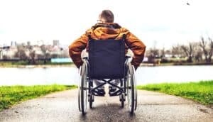 A man in a wheelchair looks over a small lake at a park.