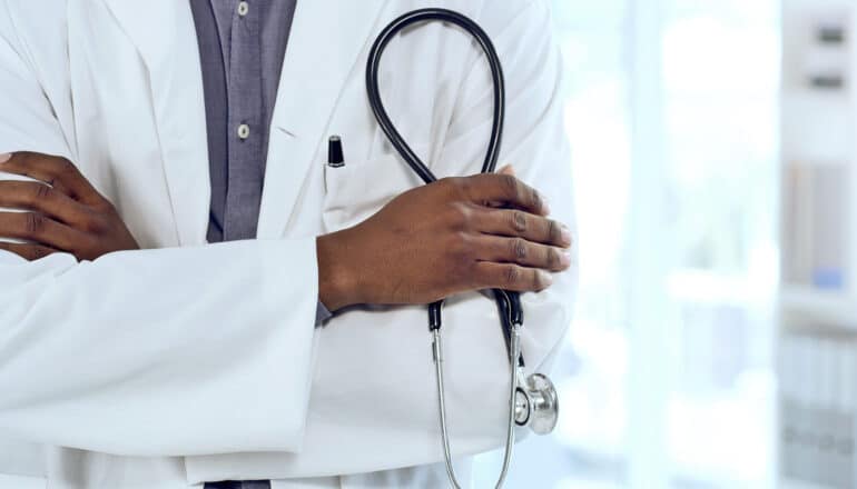 A doctor has his arms folded while holding a stethoscope in one hand.