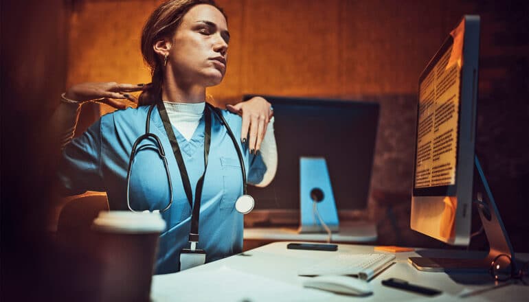 A nurse stretches while working at a computer overnight.