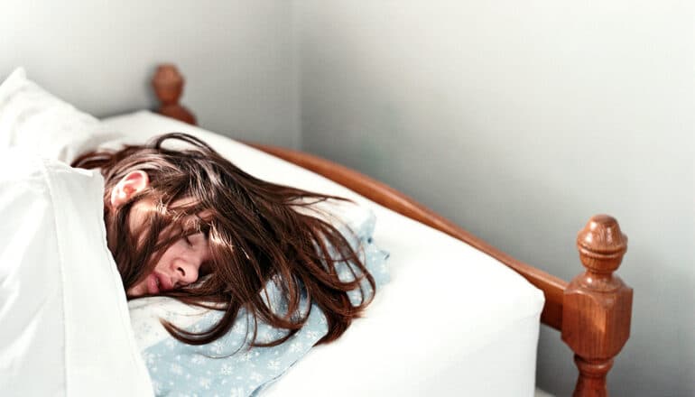 A young woman sleeps soundly in bed.