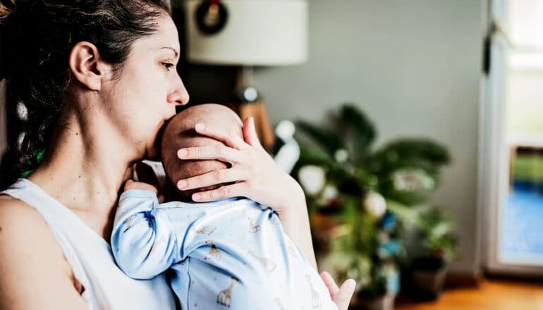 A mother holds her baby while looking overwhelmed and exhausted.