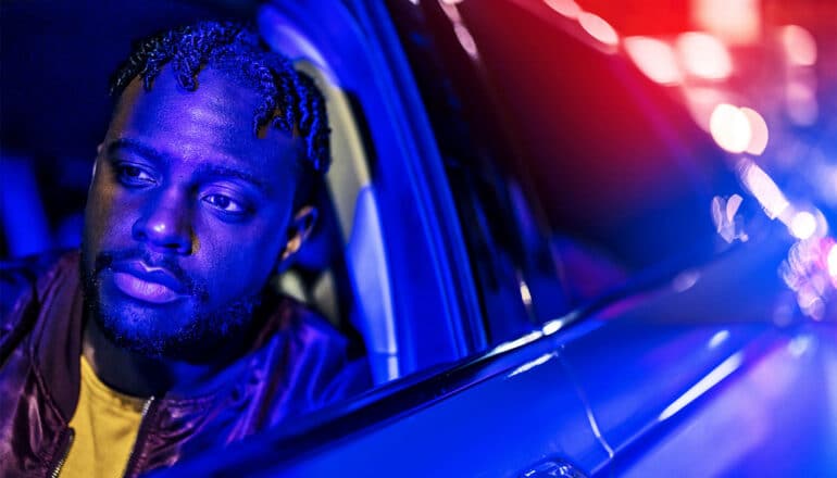 A Black man in the driver's seat of his car while being stopped by police.