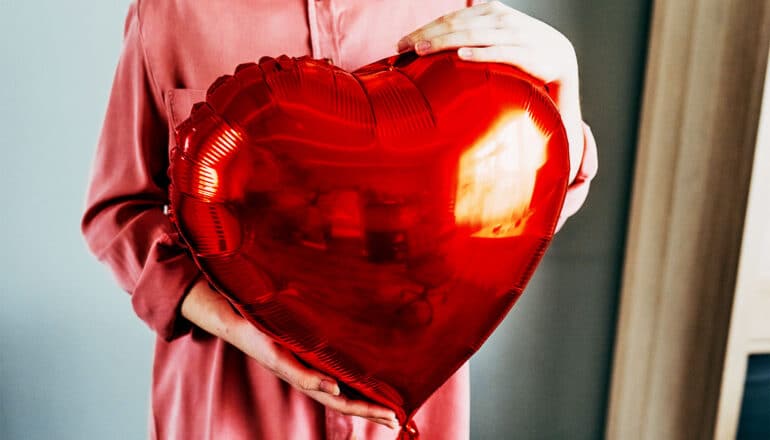 A woman holds a bright red balloon that's in the shape of a heart.