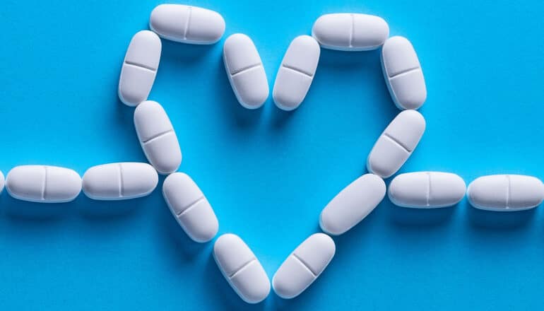 White pills arranged in the shape of a heart on a blue background.