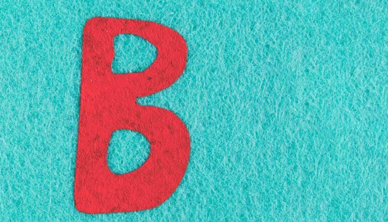 A red letter B painted on a blue felt background.