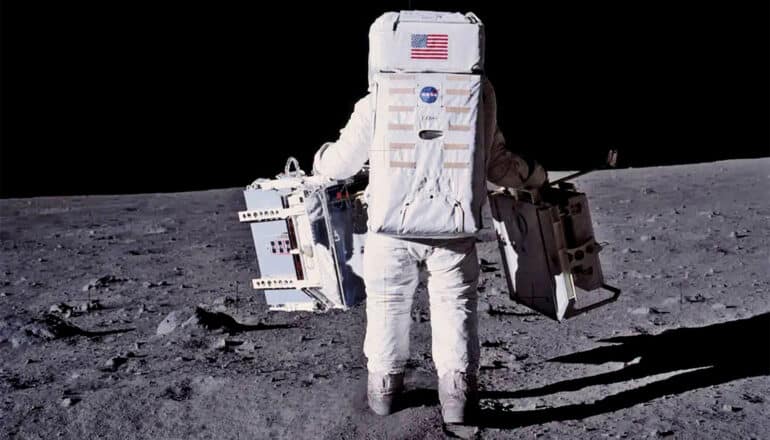 Astronaut Buzz Aldrin carries equipment as he walks on the surface of the moon.