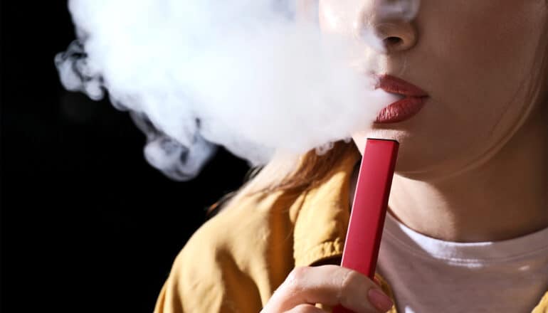 A young woman vapes from an e-cigarette.