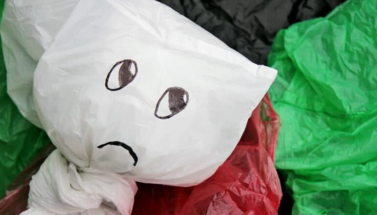 A bunch of plastic bags piled together with the foremost clear bag having a frowning face drawn on it.