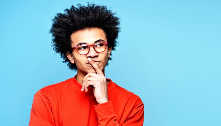 A young man puts his finger to his lips and looks off to the side while thinking deeply.