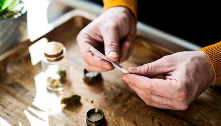 A person rolls a marijuana joint over a wooden tray.