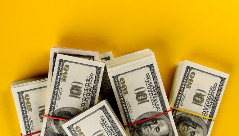 Bundles of one hundred dollar bills sit on a yellow background.