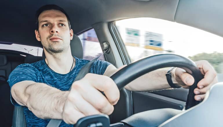 A driver grips the steering wheel and looks intently at the road.