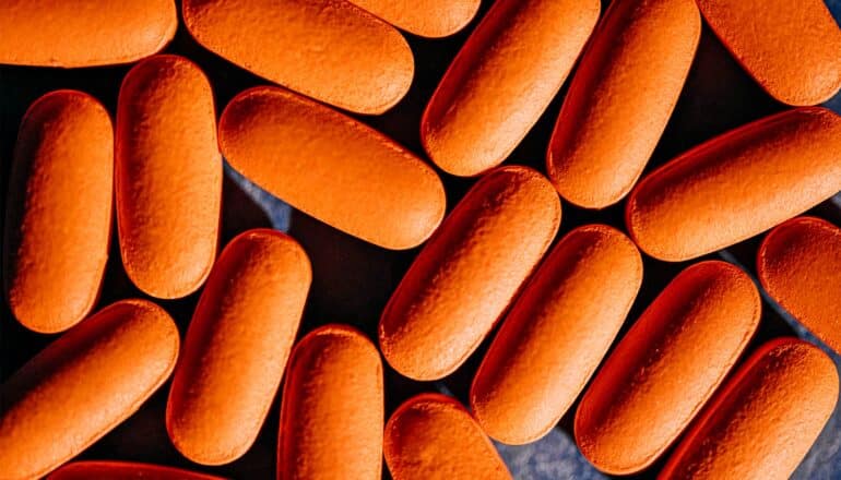 Many orange pills on a dark background.