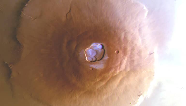 An aerial shot of a the volcano Olympus Mons on Mars with frost on the top shaded in blue.