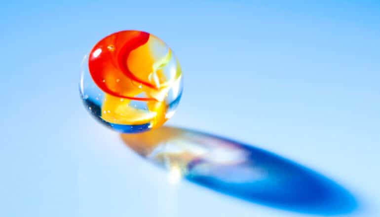 Light shines through a glass marble with red and yellow swirls in it.