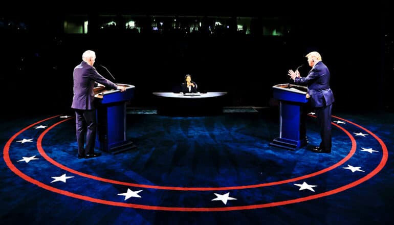 Joe Biden and Donald Trump stand at podiums facing a debate moderator.