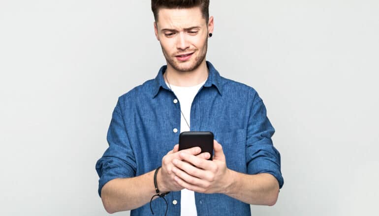 A young man looks down at his phone with a confused look.