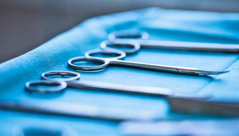 A close-up shot of surgical scissors on a tray covered in a blue cloth.