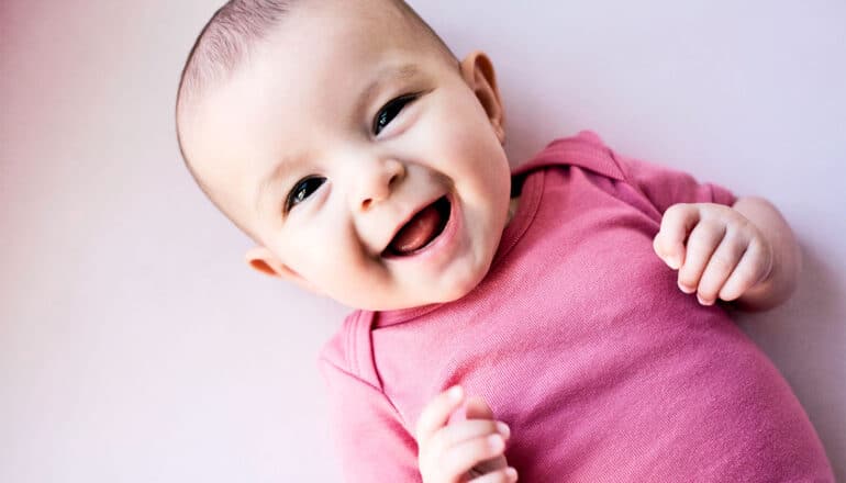 A smiling baby dressed in a pink onesie.
