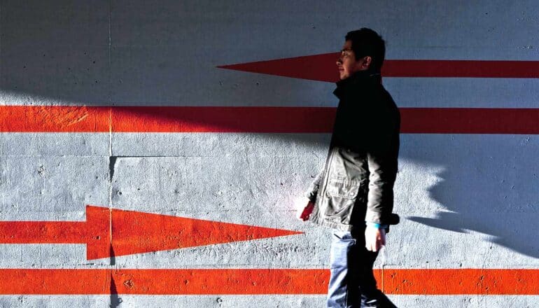 A man walks past a gray wall with red arrows pointing in both directions.