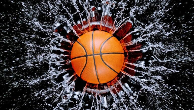 An orange basketball splashes into some water, which sprays in all directions.