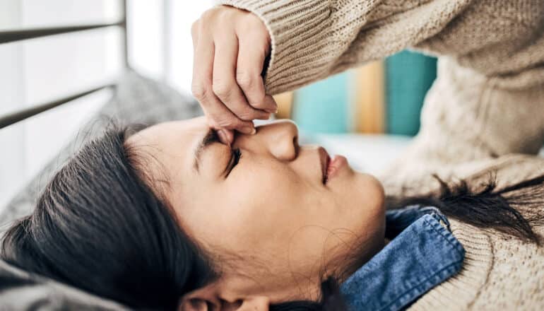 A woman holds the bridge of her nose while laying on her bed.