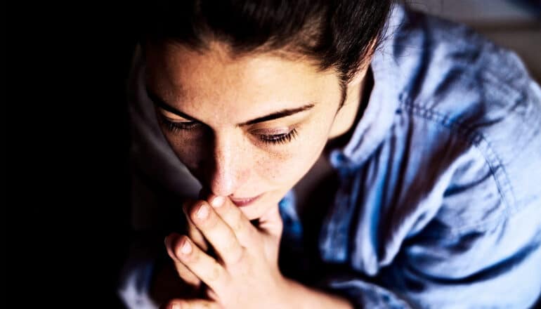 A mother clasps her hands together while looking worried.