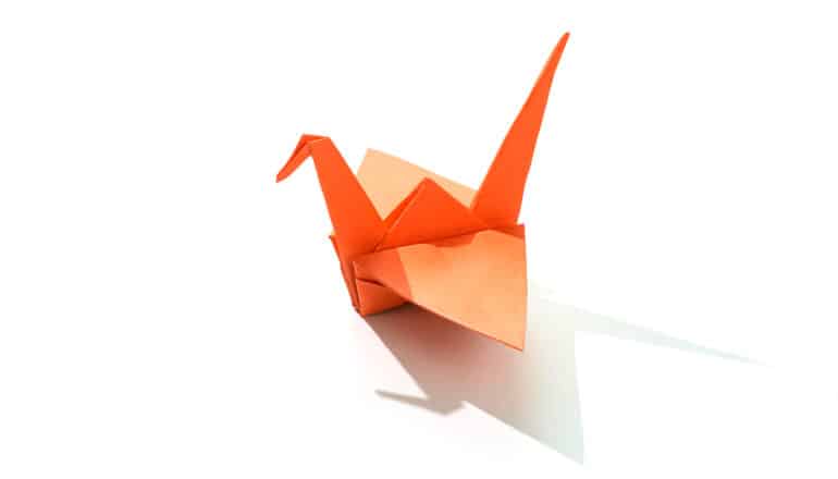 An origami crane made of orange paper sits on a white background.