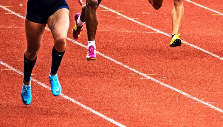 Three runners race on a reddish brown track.