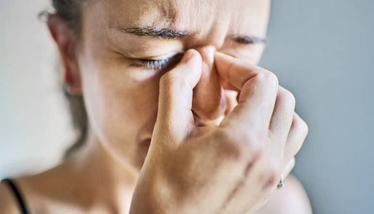 A woman holds the bridge of her nose and looks stressed.