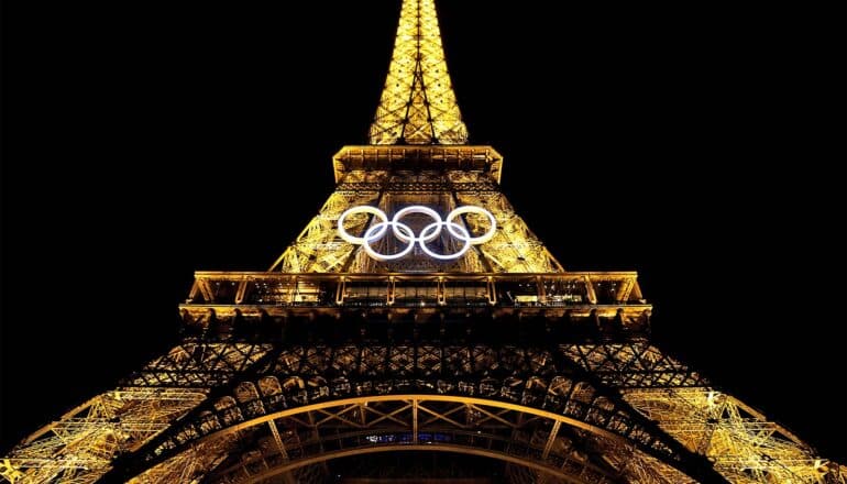 The Eiffel Tower in Paris is lighted at night and has white Olympic rings on its front.