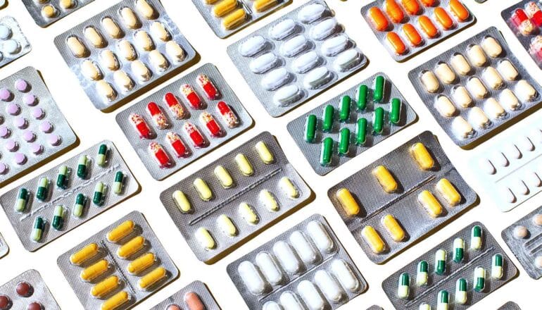 Rows of pills in silver blister packets on a white background.