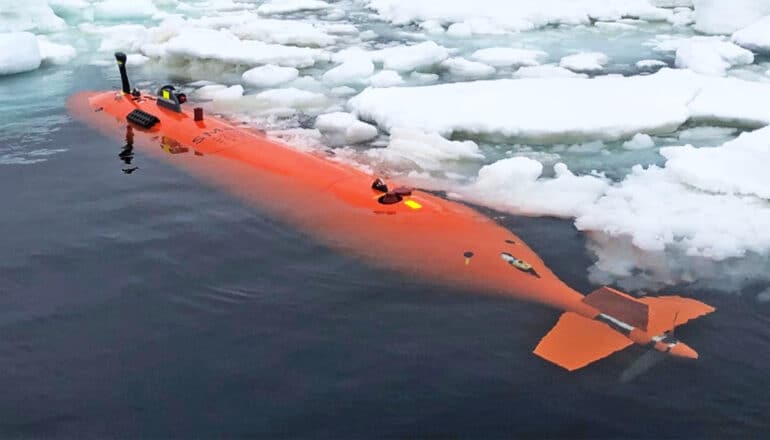 The submersible, a long orange tube with fins on the back end, sits at the water's surface near some sea ice.