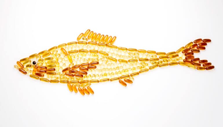 Gold and yellow fish oil capsules arranged in the shape of a fish on a white background.