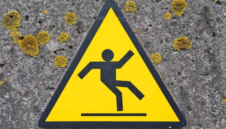 A yellow and black sign with a stick figure falling warns against the risk of falls.