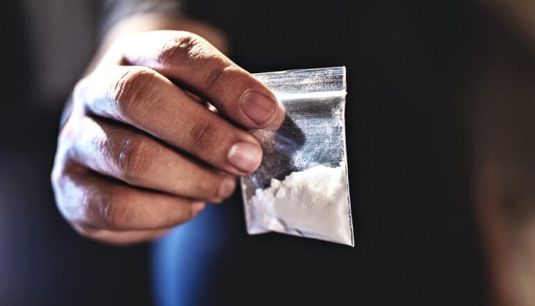 A person holds a small baggie filled with cocaine.