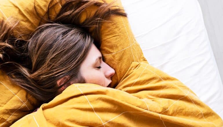 A woman sleeps under a yellow blanket in bed.