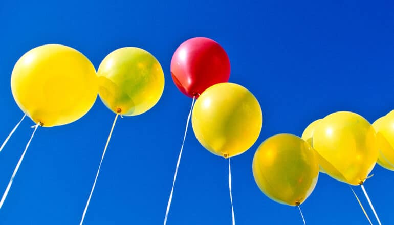 One red balloon in the middle of a row of yellow balloons.