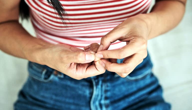 A woman picks at her nails on one hand with the other.