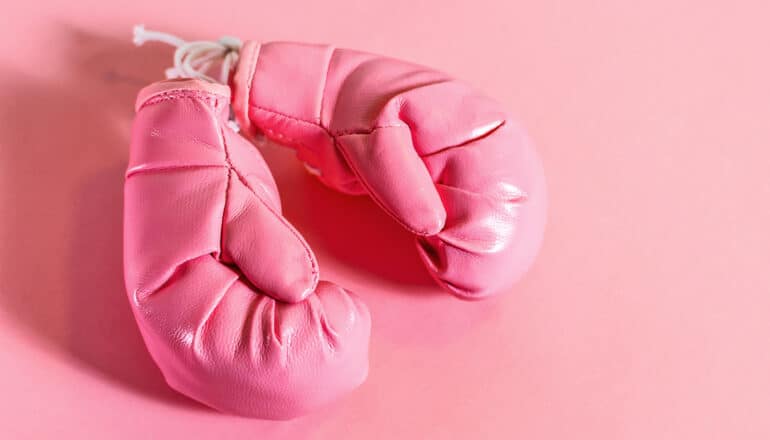 A pair of pink boxing gloves sit on a pink surface.