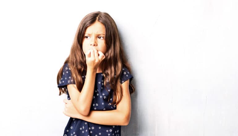 A young girl looks concerned as she bites her fingernails.