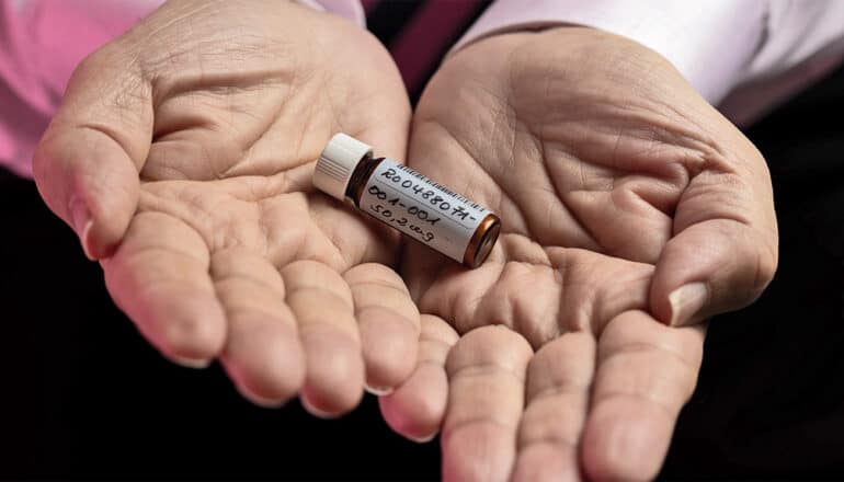 A researcher holds a small vial of the new drug for triple negative breast cancer in both of their palms.