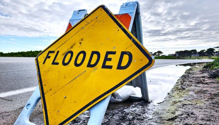 A yellow warning sign next to a road reads "Flooded."