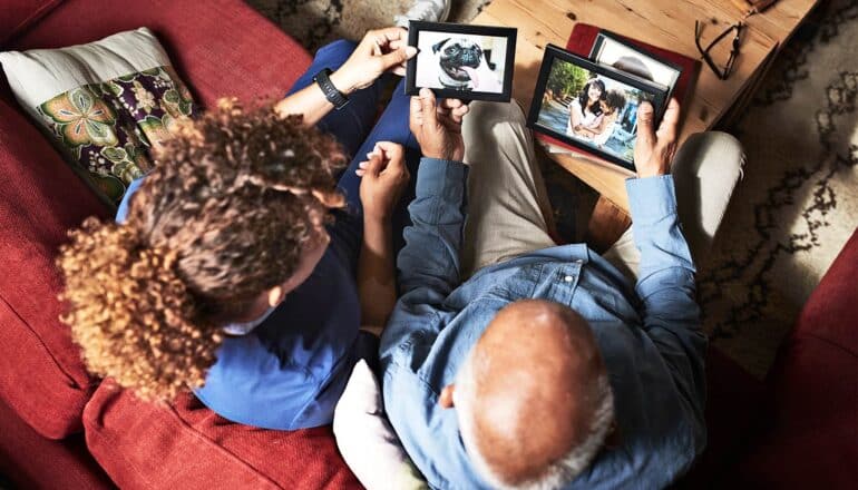 An older man and his daughter look at photos together while sitting on a couch.