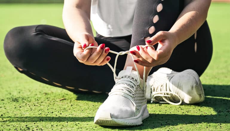 A woman sits on artificial turf while tying up her running shoes.